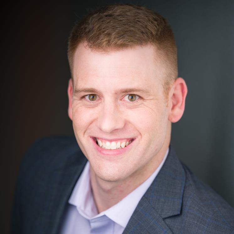 A man stood in formal attire smiling with a dark backdrop