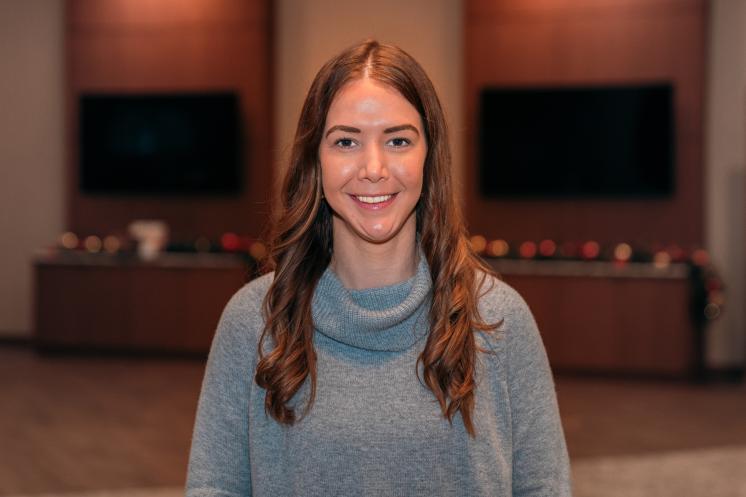 A woman standing inside posing in front of a dark background with televisions