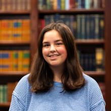 A female student standing in front of a wooden case of books.
