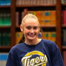 A female student standing in front of a wooden case of books.