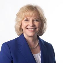 A woman in a navy blazer with blonde hair smiling
