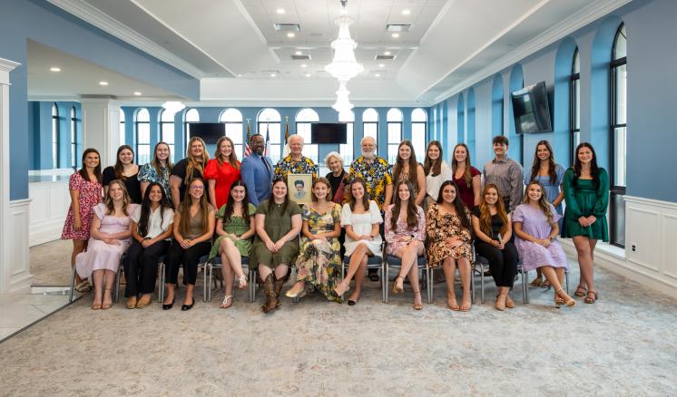A group photo of people sitting inside in a well-lit room with large windows