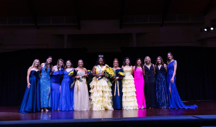 A group of women standing on a stage in formal attire
