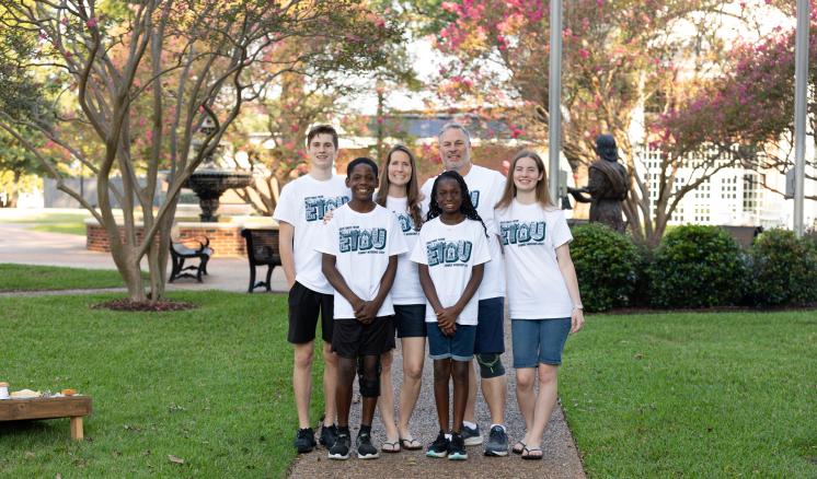 A group of people standing outside under a tree with "ETBU Family Weekend" T-Shirts
