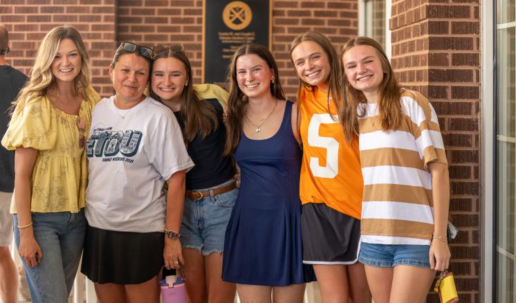 A group of women stood together in front of a brick wall, smiling