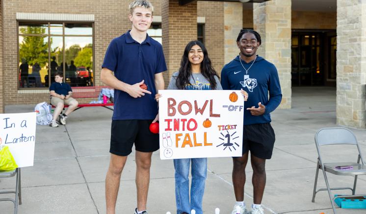 3 people outside holding a sign that says "Bowl into Fall 1 Ticket"