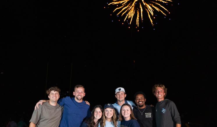 A group of people posing under a sky filled with colorful fireworks at night.