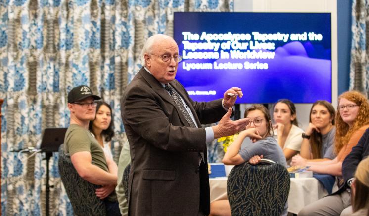 A man in formal attire speaking to a crowd sitting in a circle
