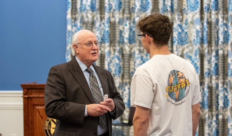 A man in formal attire speaking to a young man in a t-shirt