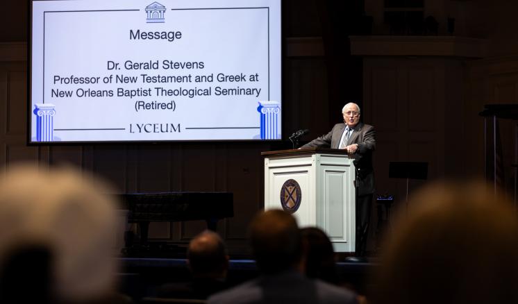 A man stood in formal attire behind a podium speaking to a crowd