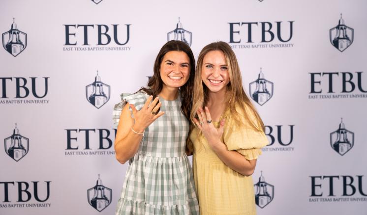 2 women standing in front of an ETBU backdrop with hands extended showing rings