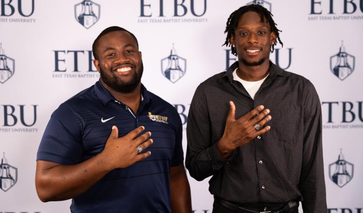 2 people standing in front of an ETBU backdrop with hands extended showing rings