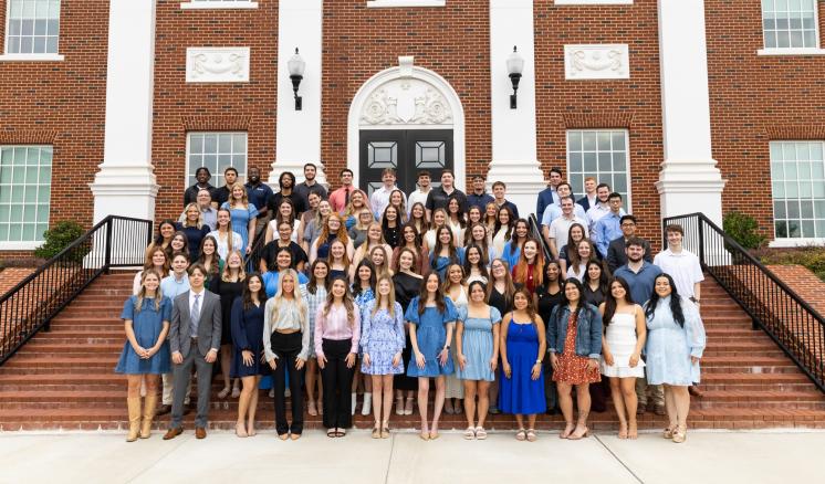A group of people standing on the steps of a large brick building with white collumns