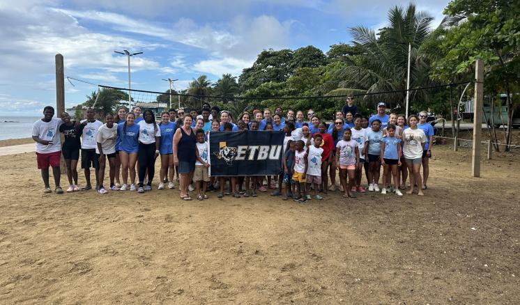 A group of people holding an ETBU flag on the beach outside