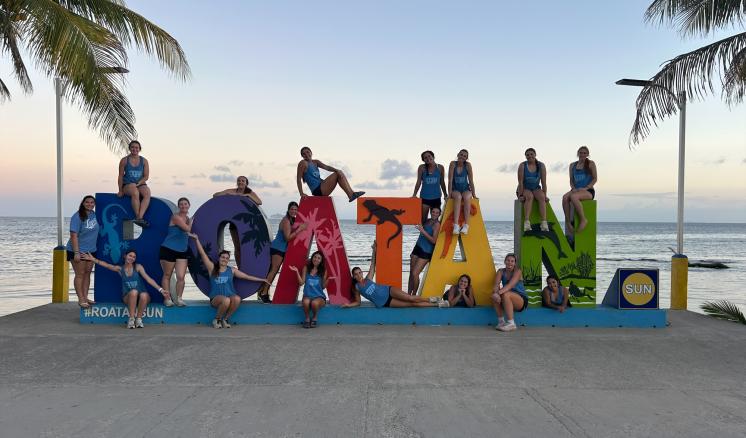 A group of people standing on and around the Roatan sign