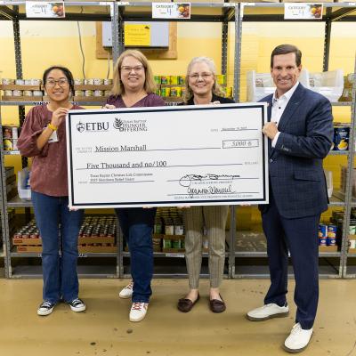 4 people holding a giant check inside a warehouse
