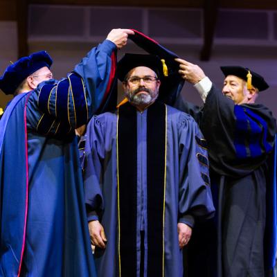 2 men hooding another all wearing academic regalia