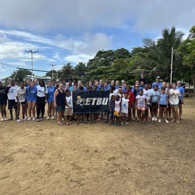 A group of people holding an ETBU flag on the beach outside
