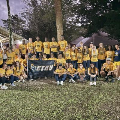 a group of people outside in yellow shirts holding an ETBU flag