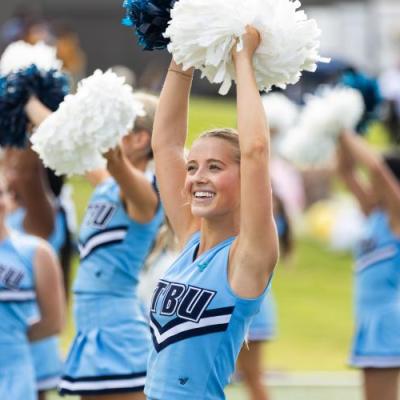 Cheerleader stands smiling with pom poms raised in the air 