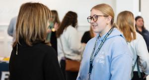 2 people talking with a group of people behind them inside