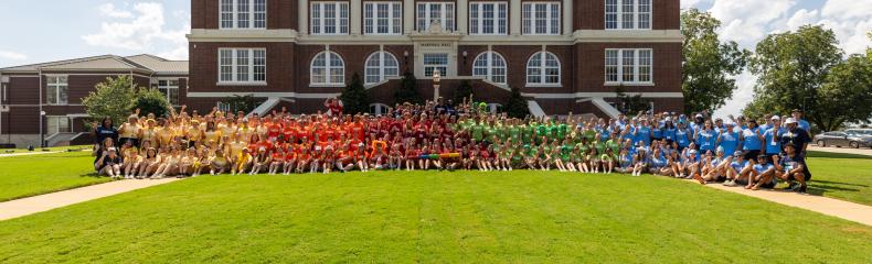 A group photo of a large group of student standing in front of a brick building