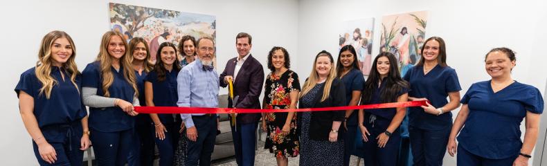 A group of people stood in a room with large scissors cutting a bright red ribbon