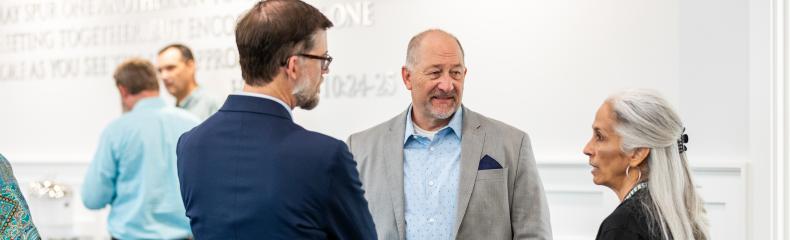 A group of three people, two males and one woman, indoors in a white-walled room talking.
