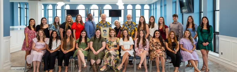 A group photo of people sitting inside in a well-lit room with large windows