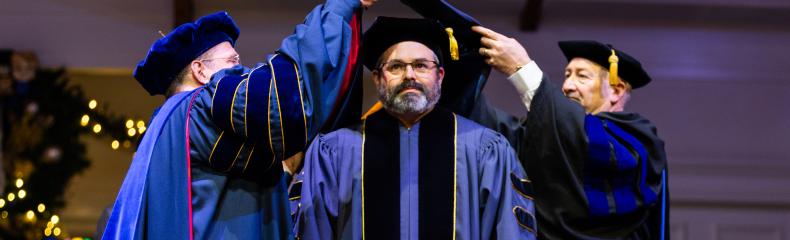 2 men hooding another all wearing academic regalia