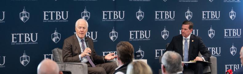 2 men sitting on a stage for a Q&A taking questions. Dressed in professional attire