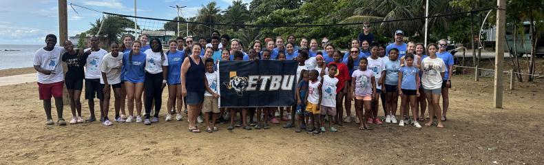 A group of people holding an ETBU flag on the beach outside
